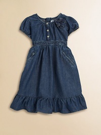 An adorable denim day dress accented with a darling floral detail and silvertone snaps.Jewel necklineCap sleeves with elasticized cuffsFront snap placketConcealed back zip closureElasticized waistbandSide slash zip pocketsRuffle hem65% cotton/35% polyesterMachine washImported