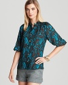 An elegant, silk-spun Trina Turk blouse featuring a hypnotic print and stylish three-quarter sleeves.